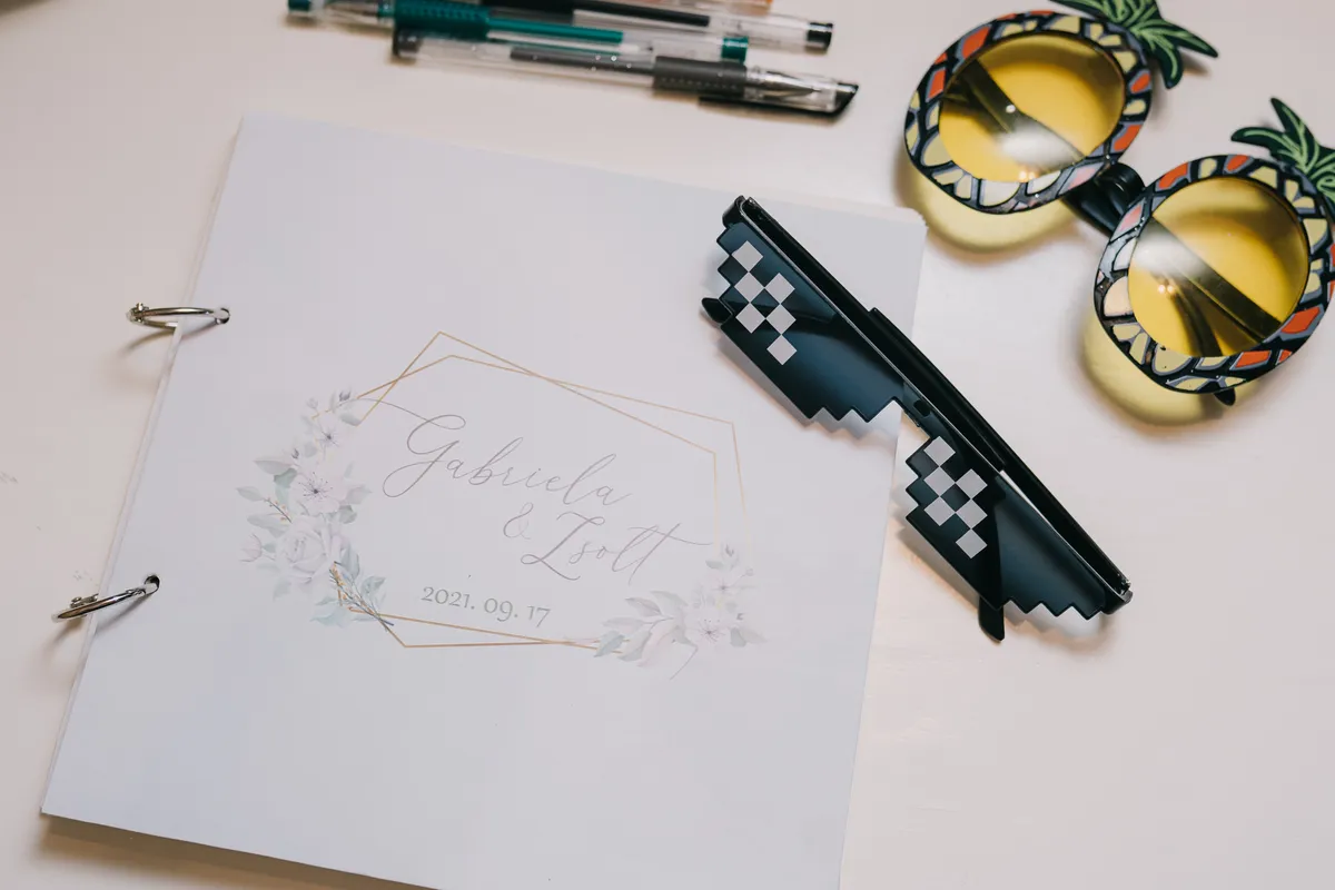 Copertă de guestbook personalizată, cu ramă aurie și numele mirilor, alături de pixuri colorate